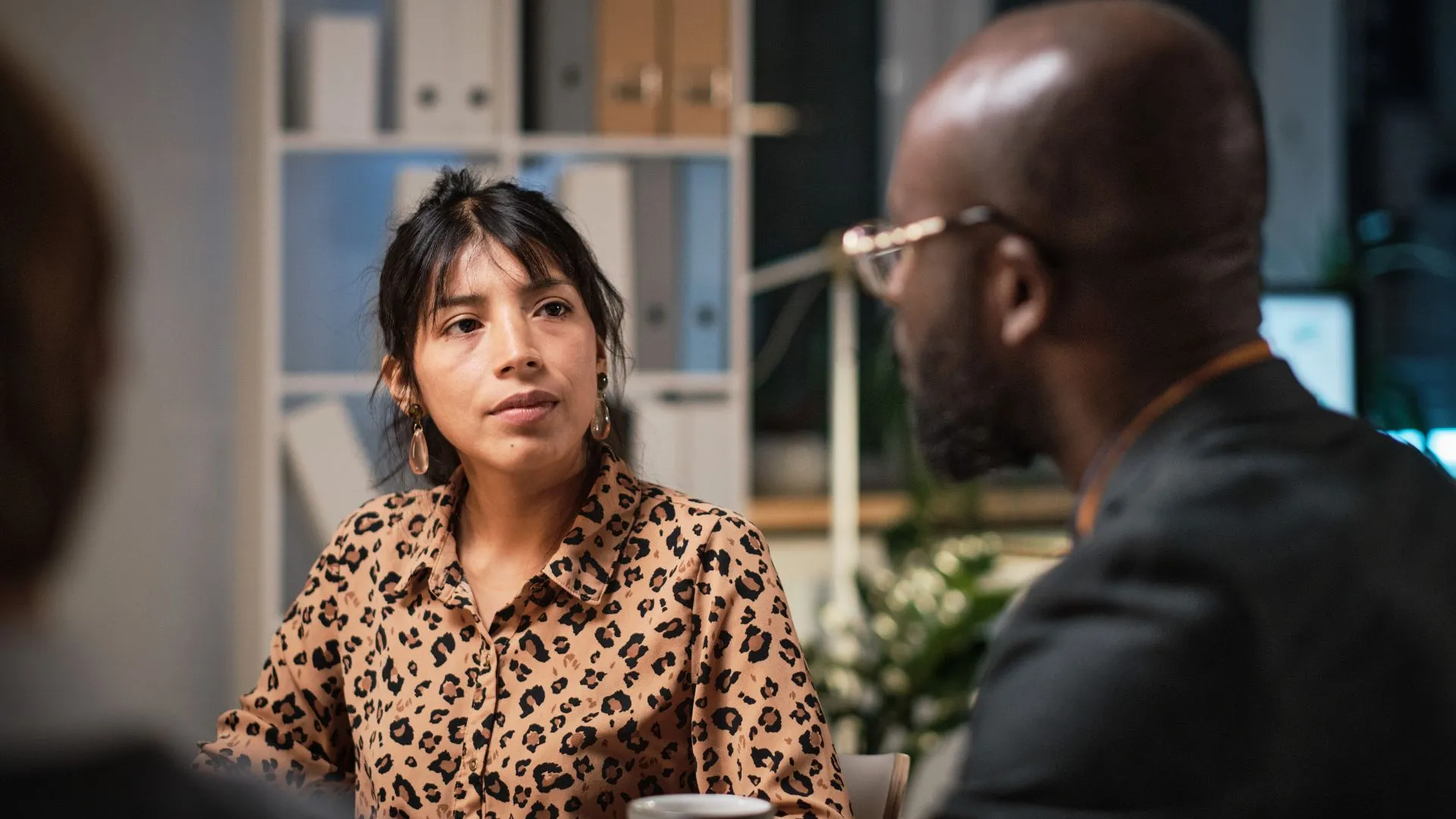 A woman wearing a leopard-print blouse attentively listens to a man during a discussion, exemplifying how she’s following a framework for receiving feedback in a professional setting.