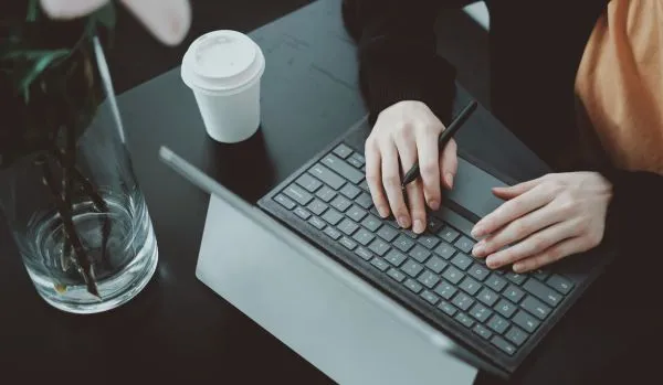 We're looking down at a woman using her laptop on a table with her coffee and a vase of flowers.