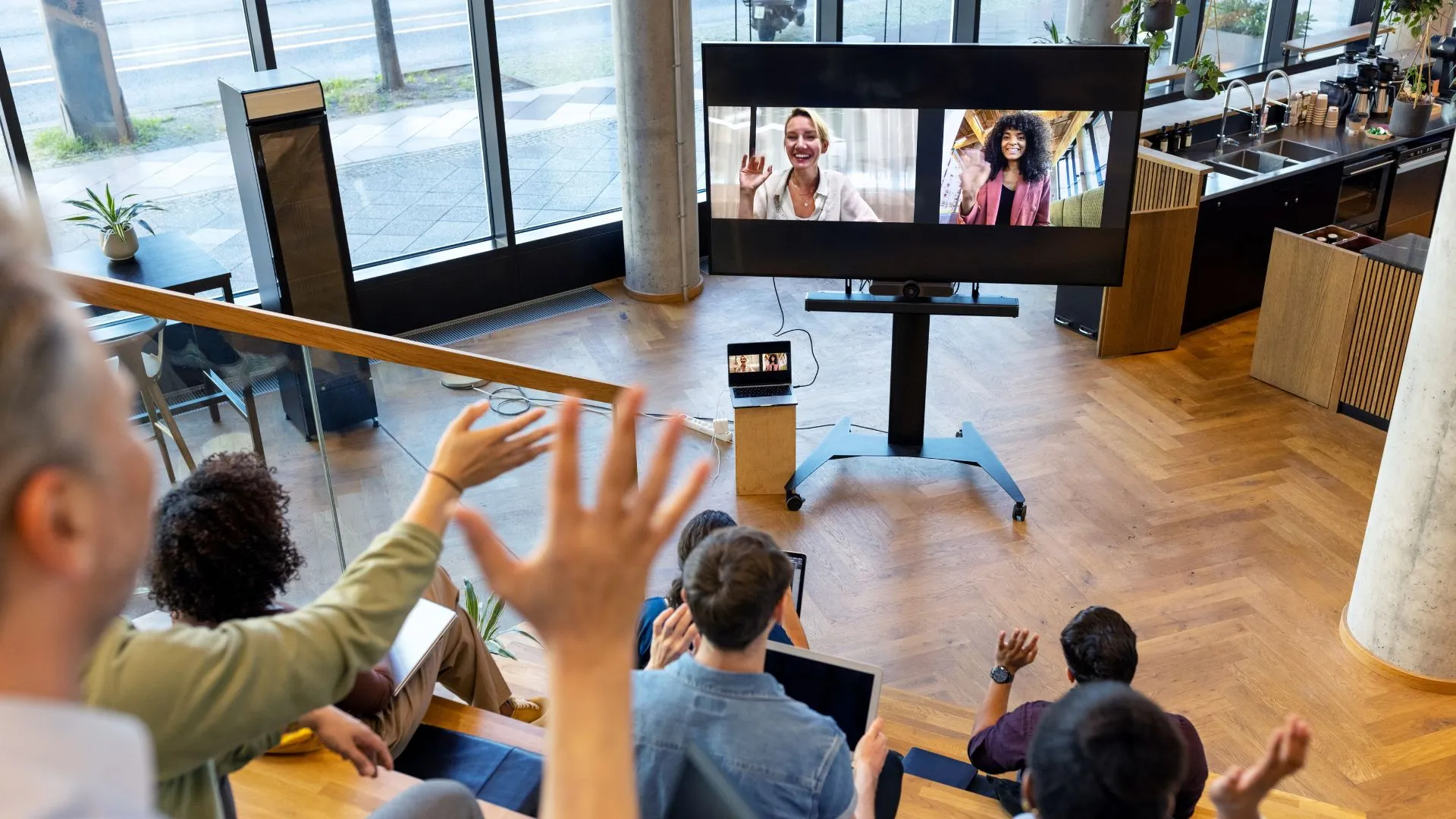 An in-office team is waving at remote workers who are video-ing into their event.