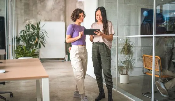 Two women are analyzing workforce trends on a tablet. They are standing in an office.