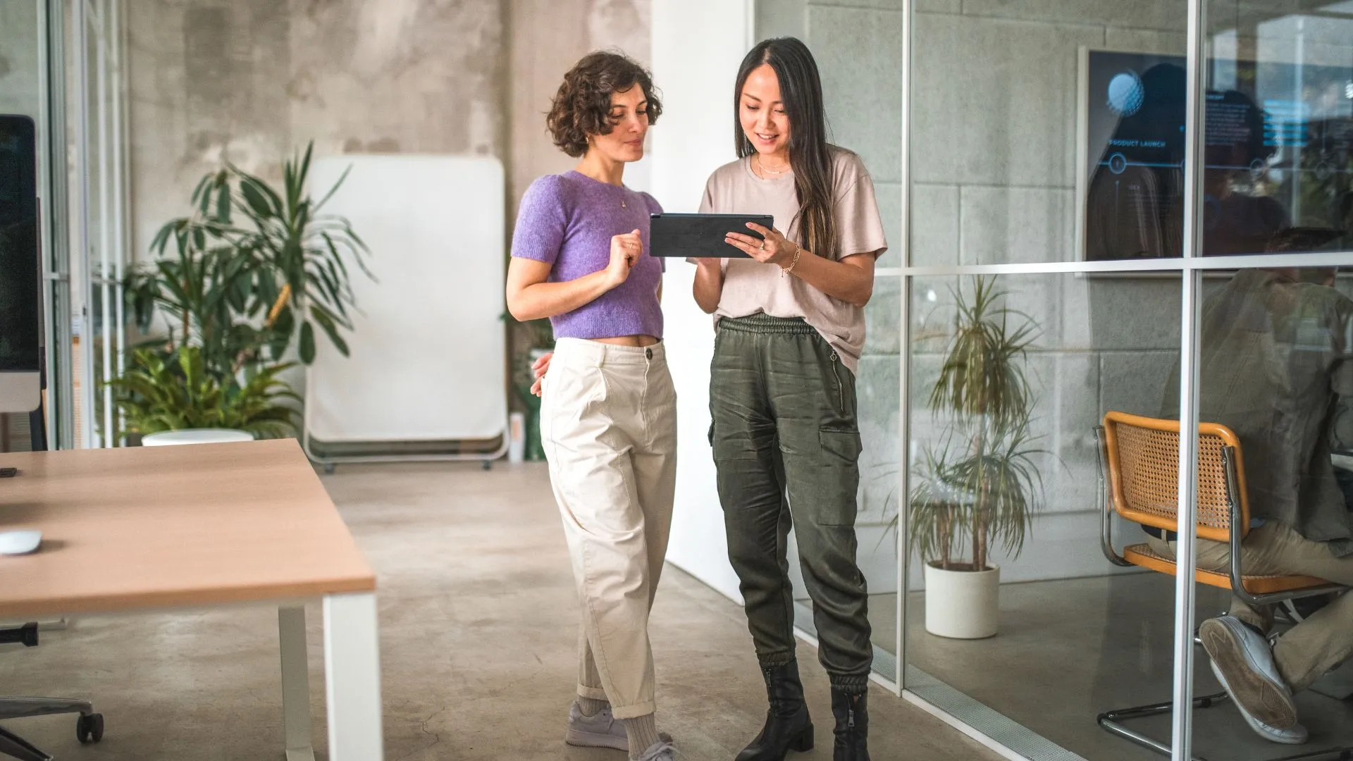 Two women are analyzing workforce trends on a tablet. They are standing in an office.