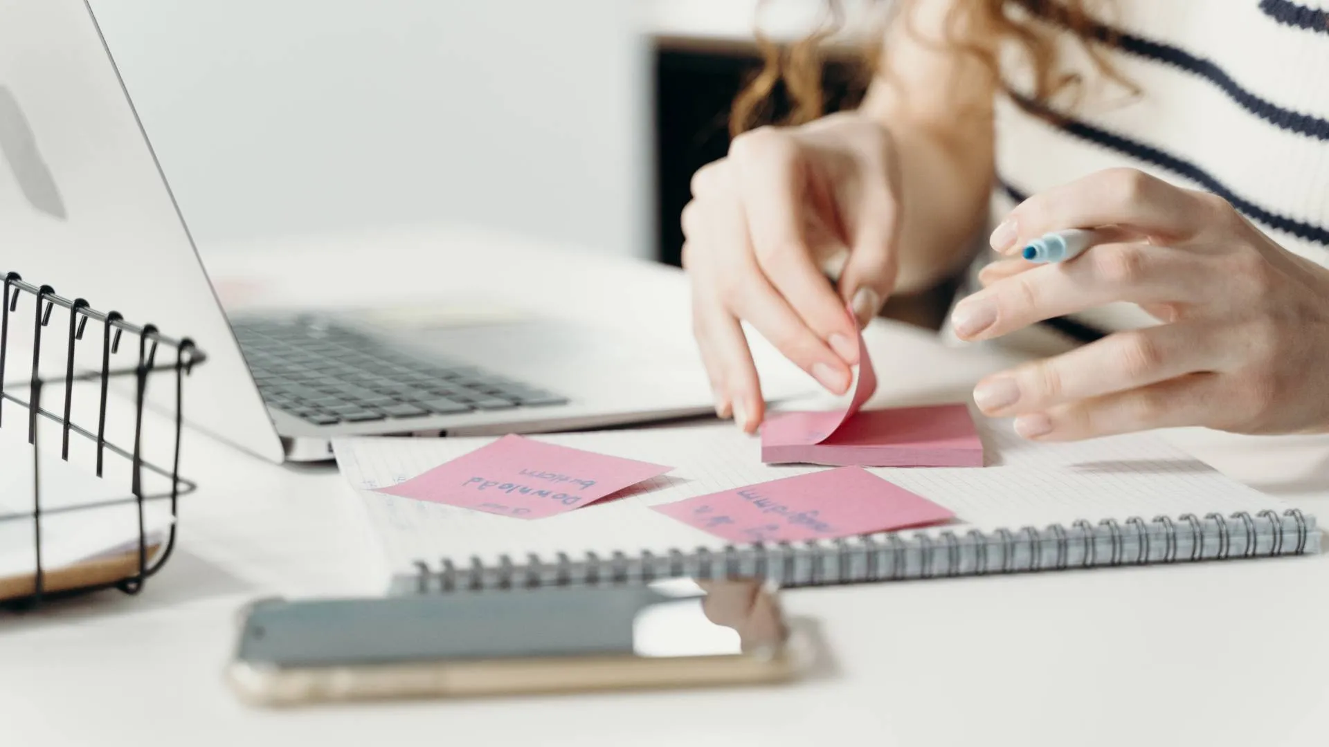 We are looking at a woman's hands as she makes notes on post-its at her desk.