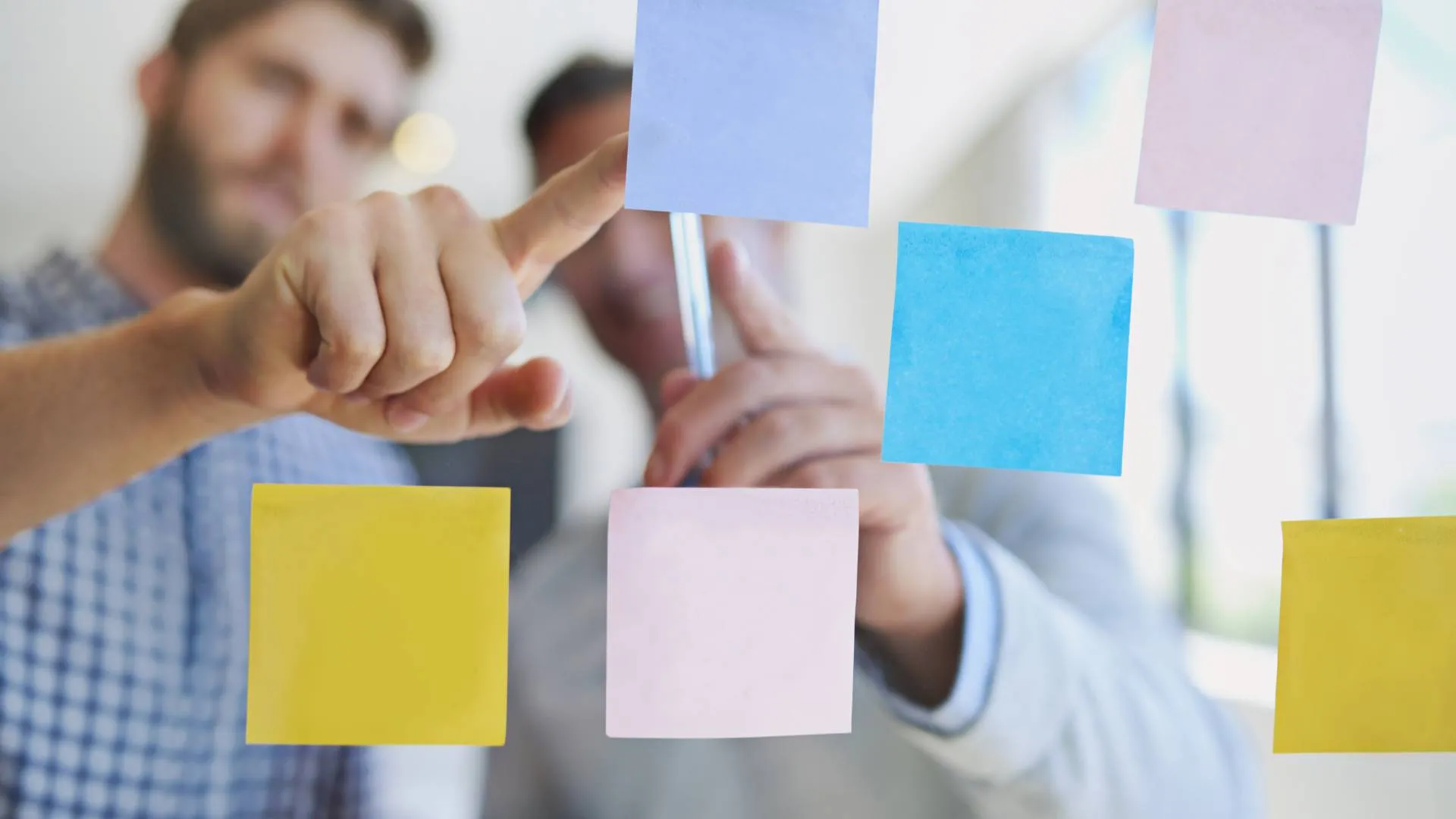 We're looking through a clear whiteboard at two people discussing a series of post-it notes as part of their design thinking process.
