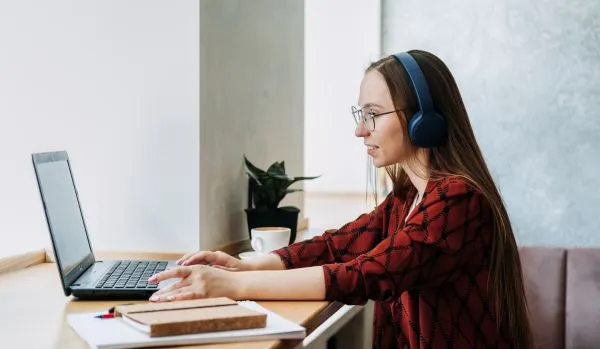 A young woman is participating remotely in a professional development program. She is sitting in front of her laptop with headphones on.