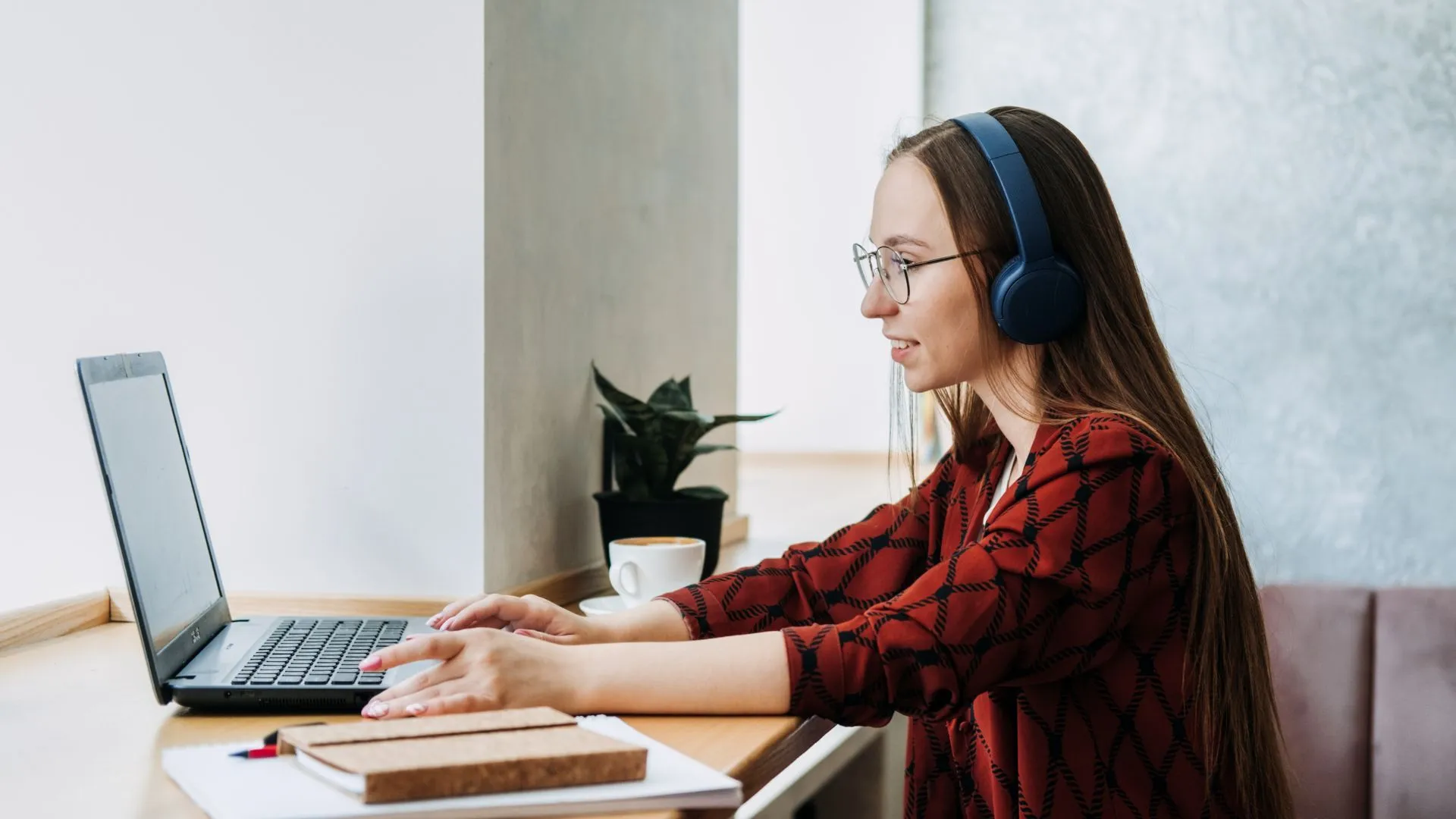 A young woman is participating remotely in a professional development program. She is sitting in front of her laptop with headphones on.