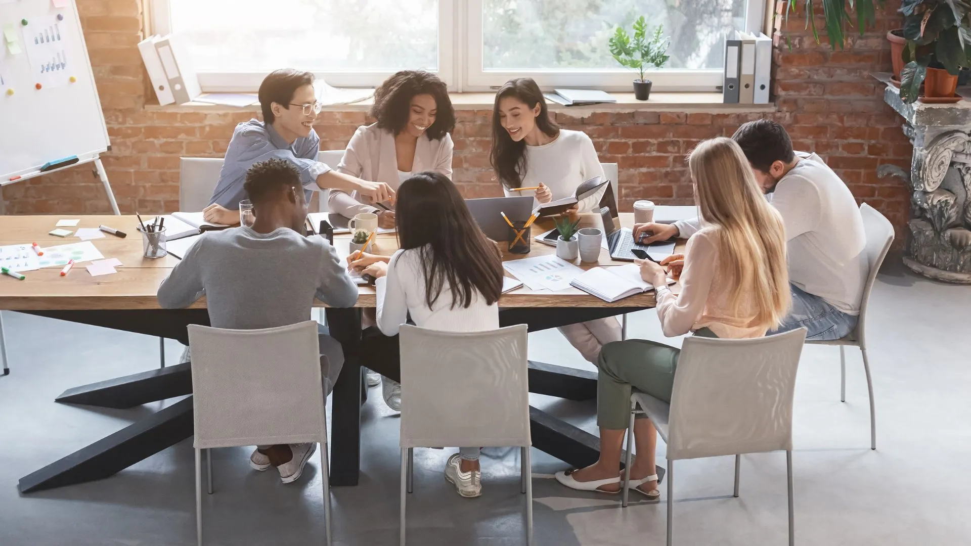 A diverse group of employees are working together on a project around a conference table with a window in the background.