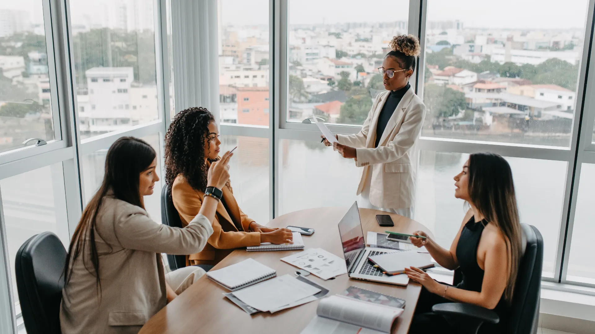 A female presenting leadership team is working together in a conference room with many windows.