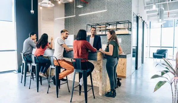 A diverse group of employees is hanging out in the open concept kitchen of their office.