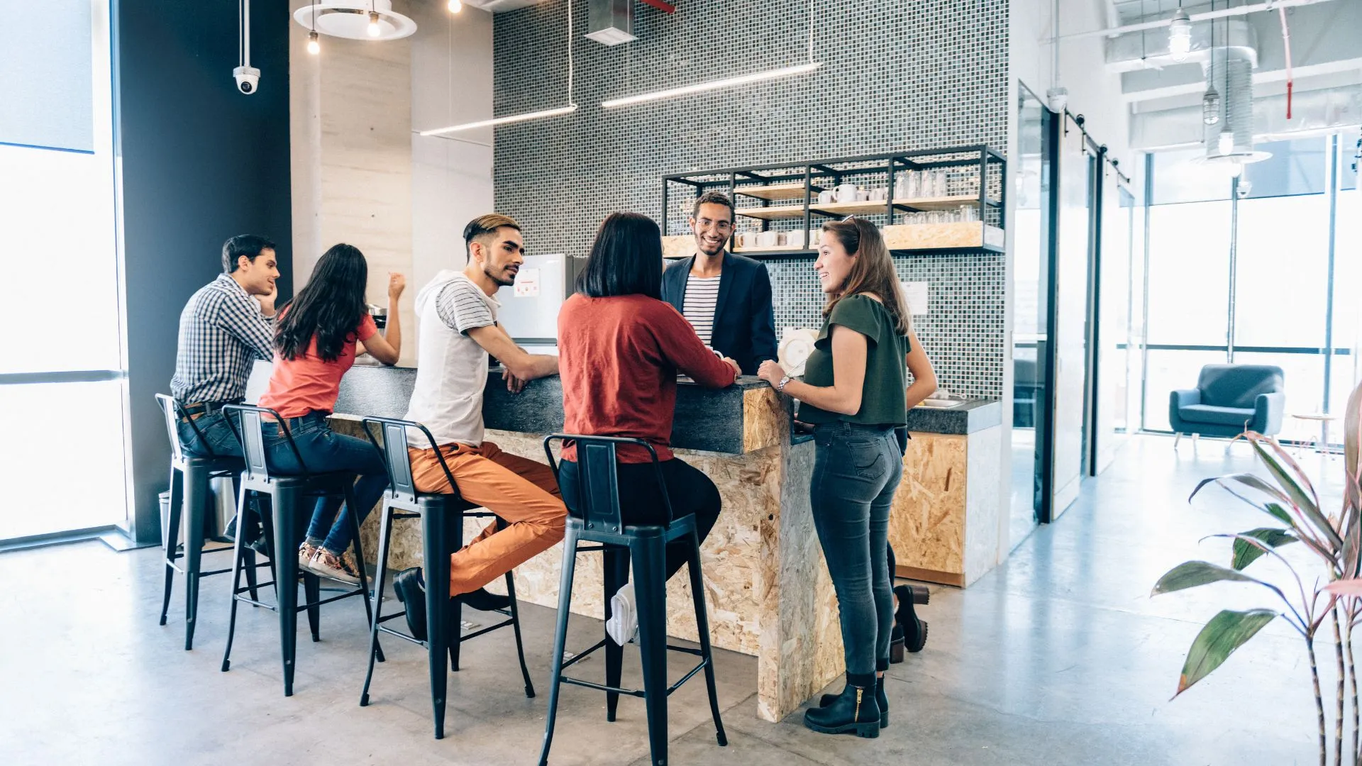 A diverse group of employees is hanging out in the open concept kitchen of their office.