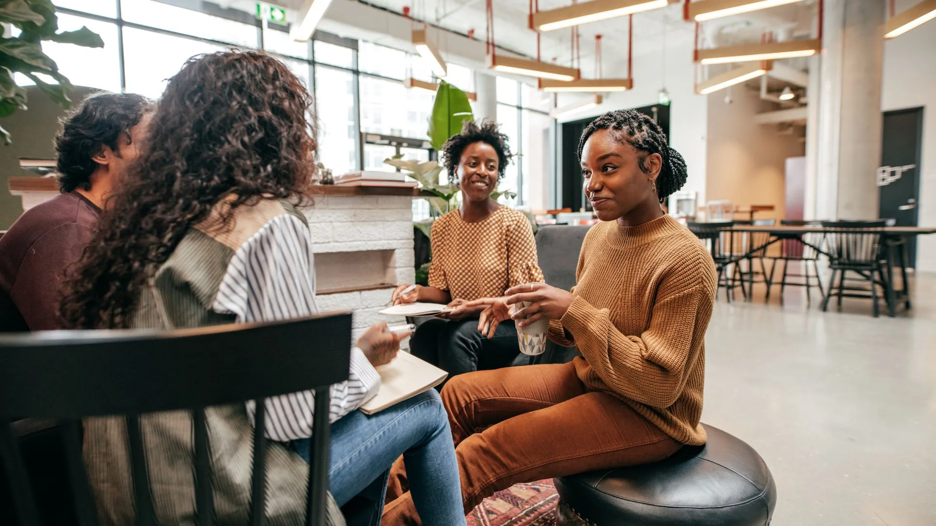 A diverse team of young workers are sitting in an open common area conversing.