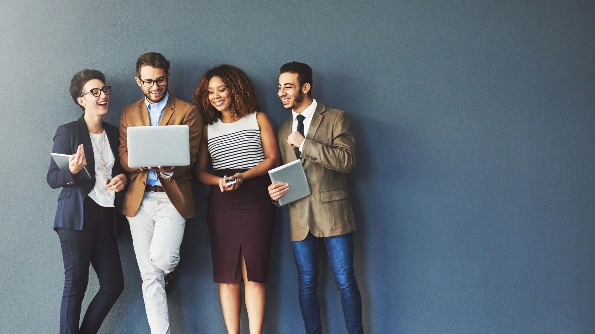 A group of four hispanic professionals are looking at a laptop and laughing. 