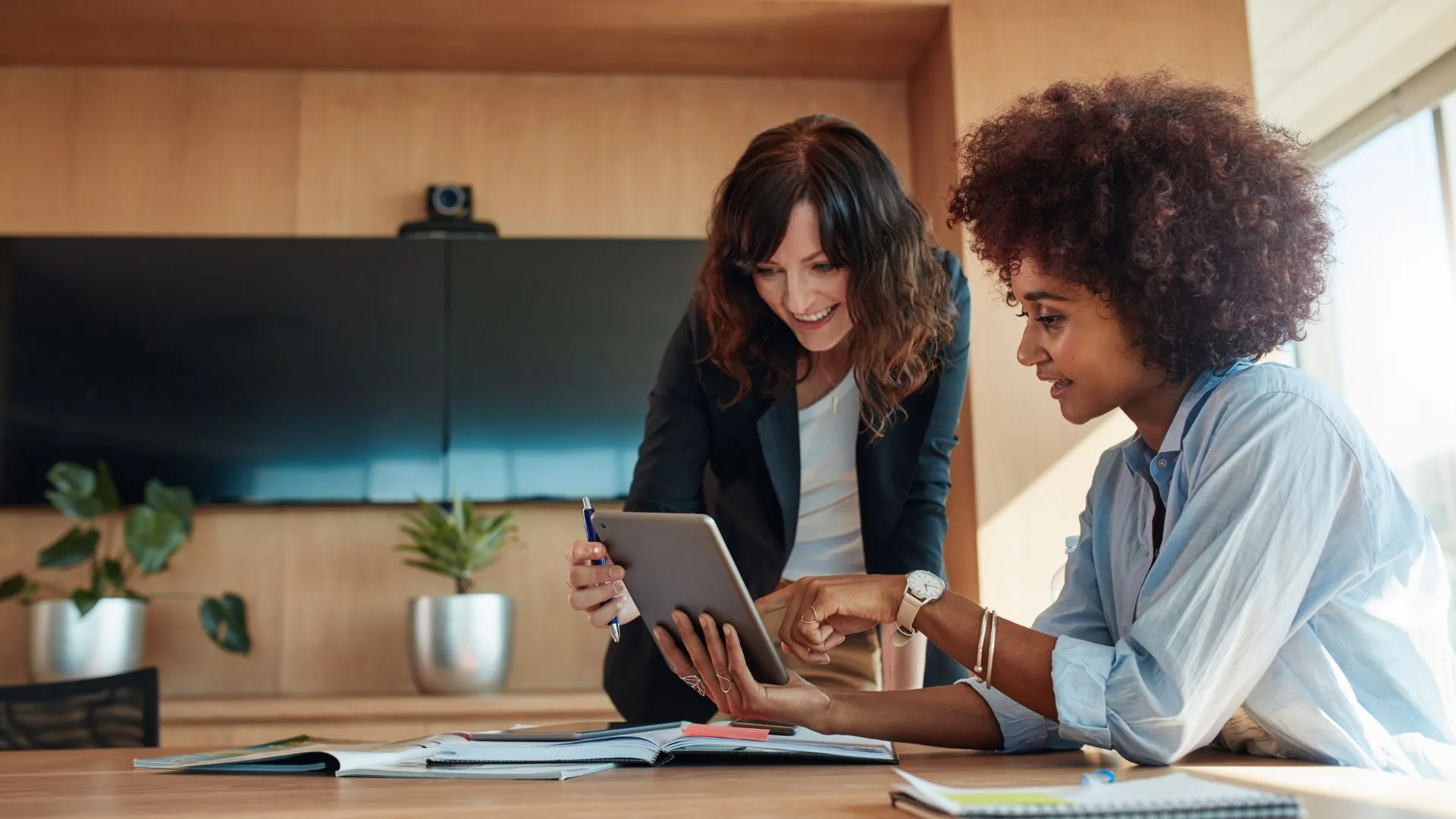 Two women are looking at a tablet and smiling n an office. 