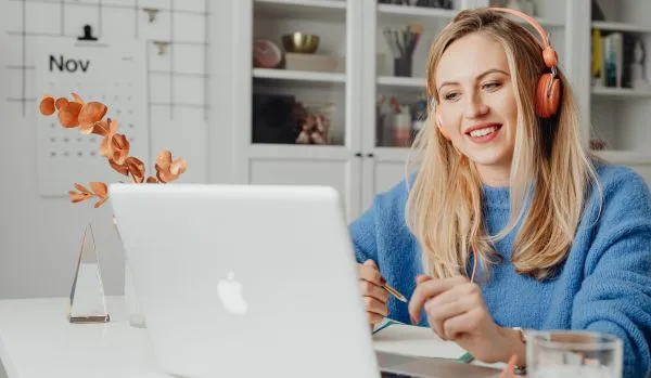 A young woman is working from her kitchen on her laptop with headphones on.