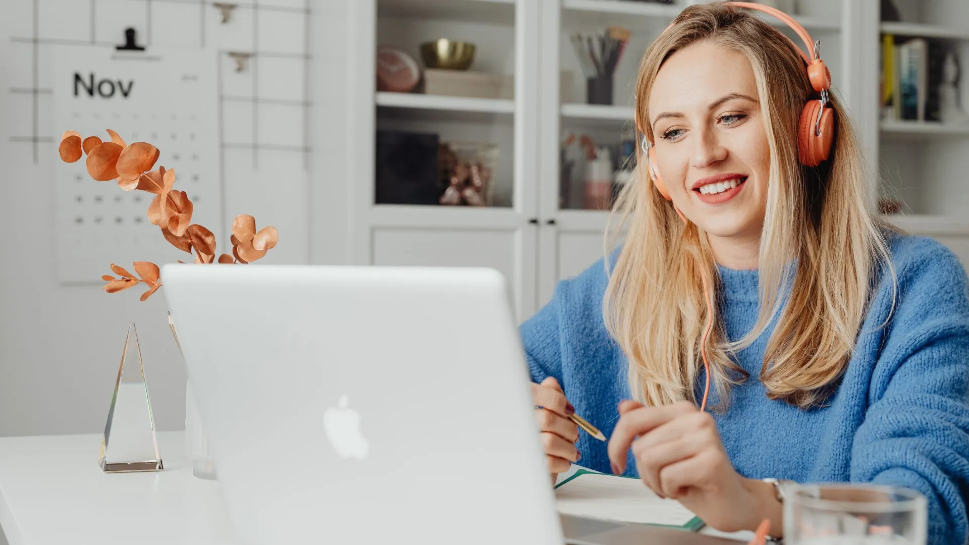 A young woman is working from her kitchen on her laptop with headphones on.