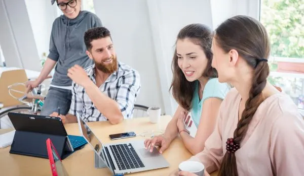 A happy team of people are experimenting with AI in their office on their laptops.