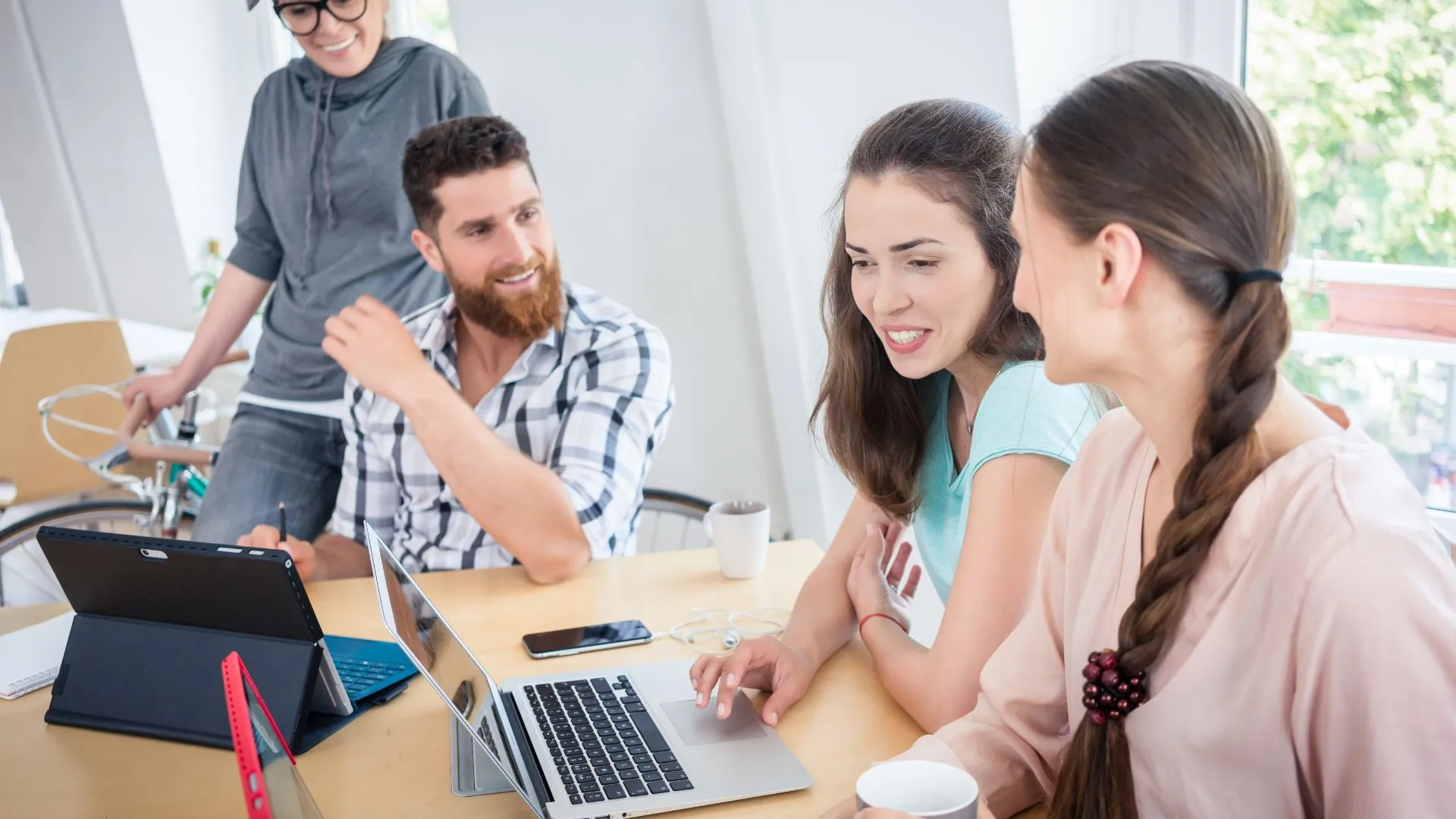 A happy team of people are experimenting with AI in their office on their laptops.