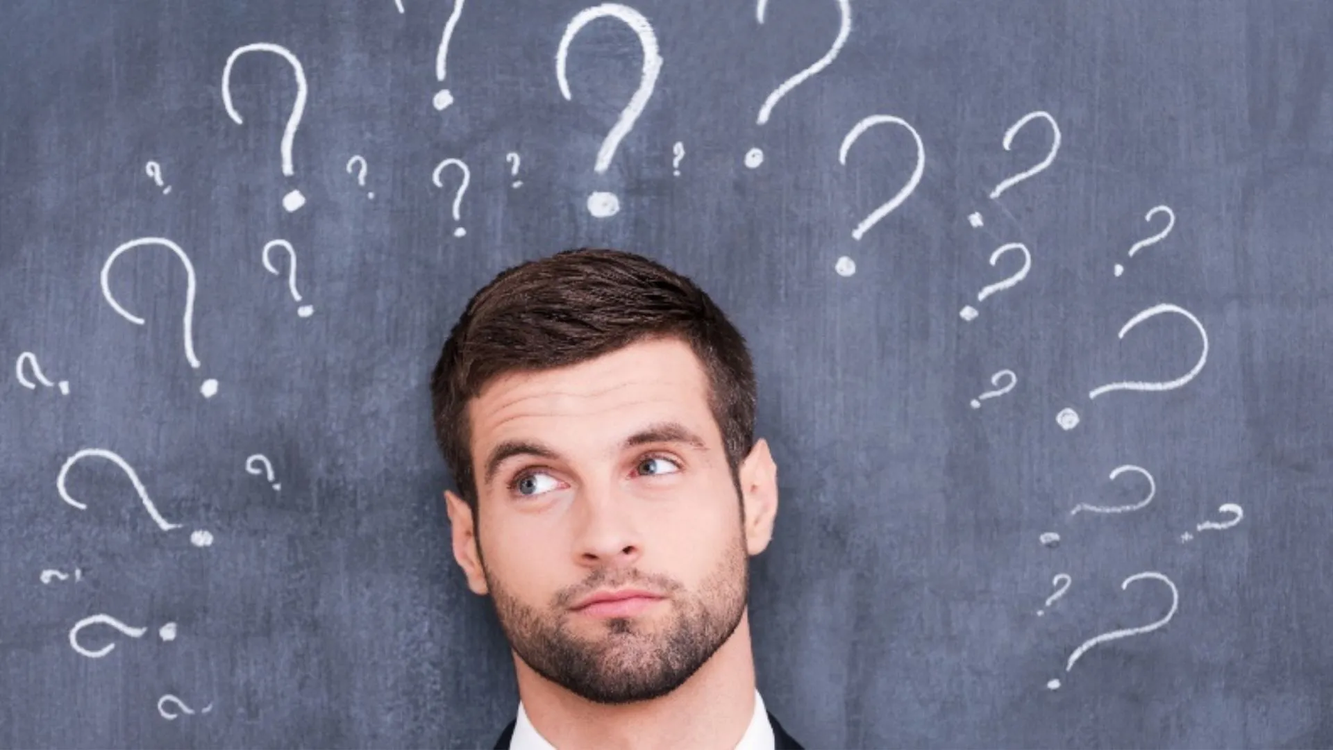 Man looking up at chalk-drawn question marks on a blackboard, symbolizing asking questions in the AI era.