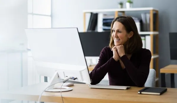 A female-presenting executive is working on a computer in her home office with a bookshelf behind her.