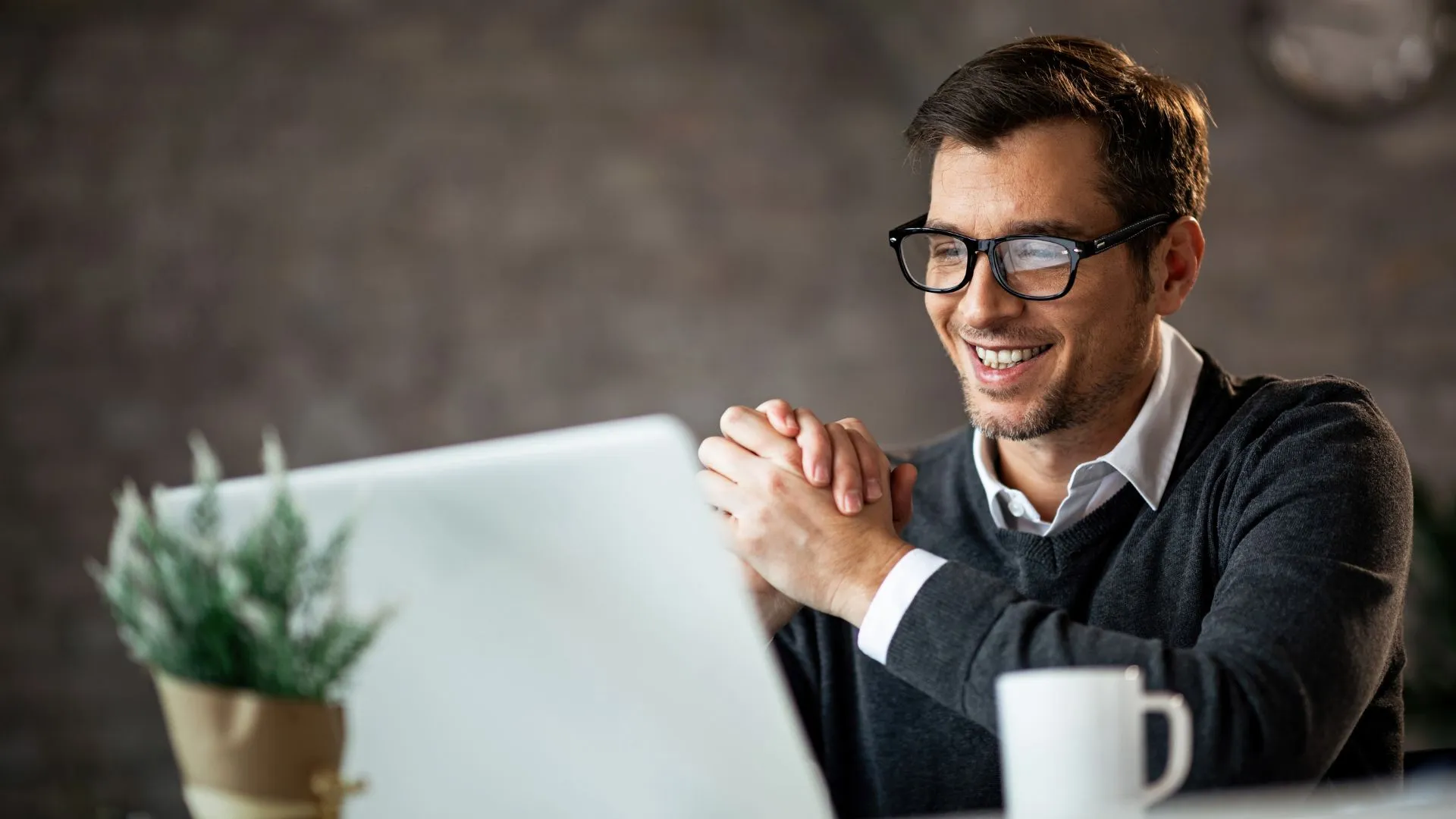 A young man in glasses id smiling down at his laptop screen.