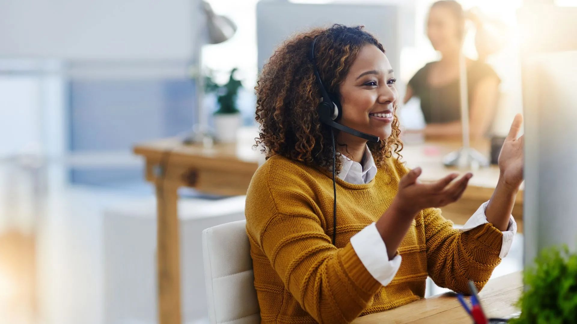 A young woman is talking on a headset sitting at her desk closing a sale.