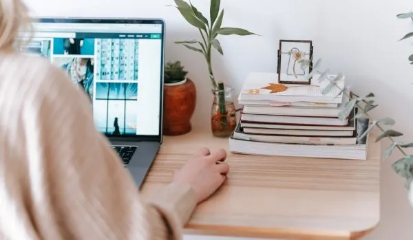 We are looking over a woman's shoulder as she uses her laptop on her desk at home.