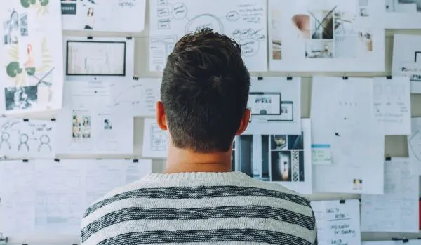 A man is standing in front of a board covered in brainstorming ideas. We are looking at the man's back.
