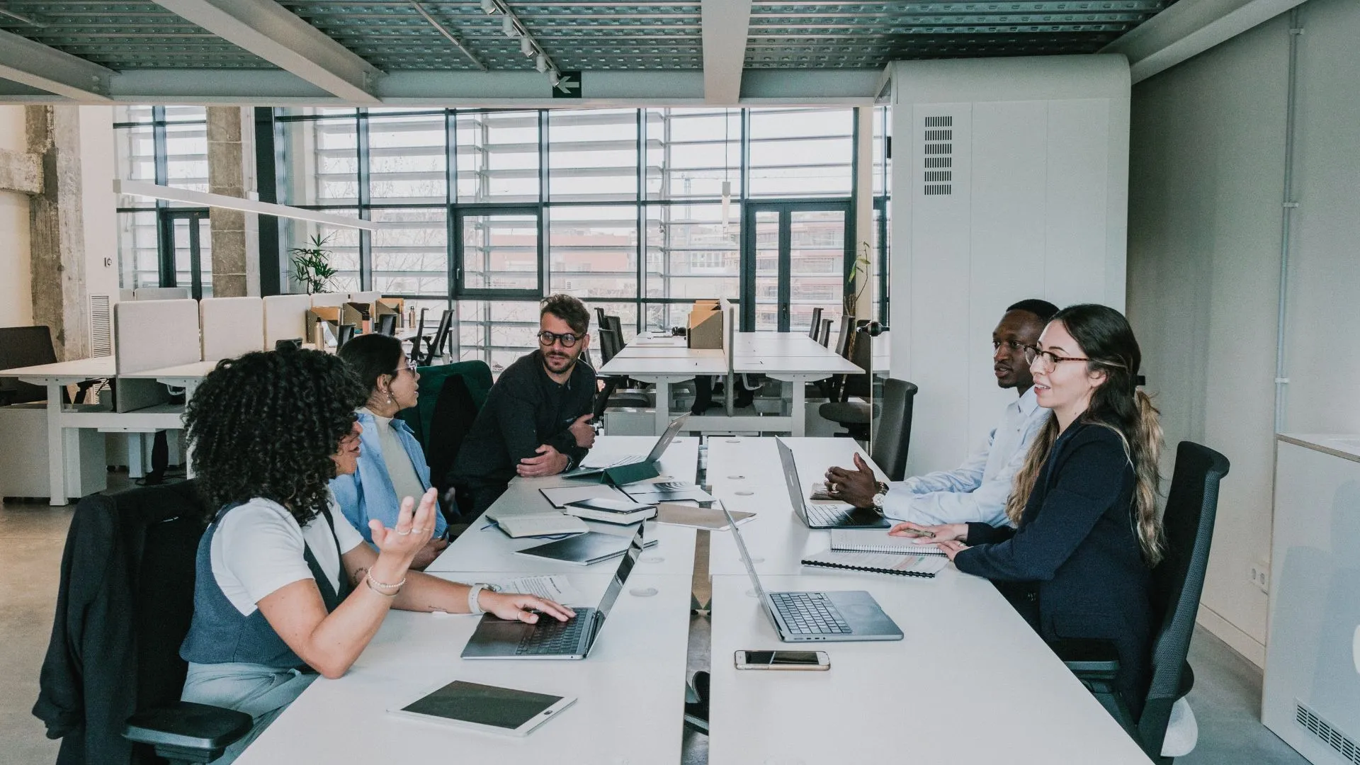 A diverse team of people are working around a conference table and having conversations.