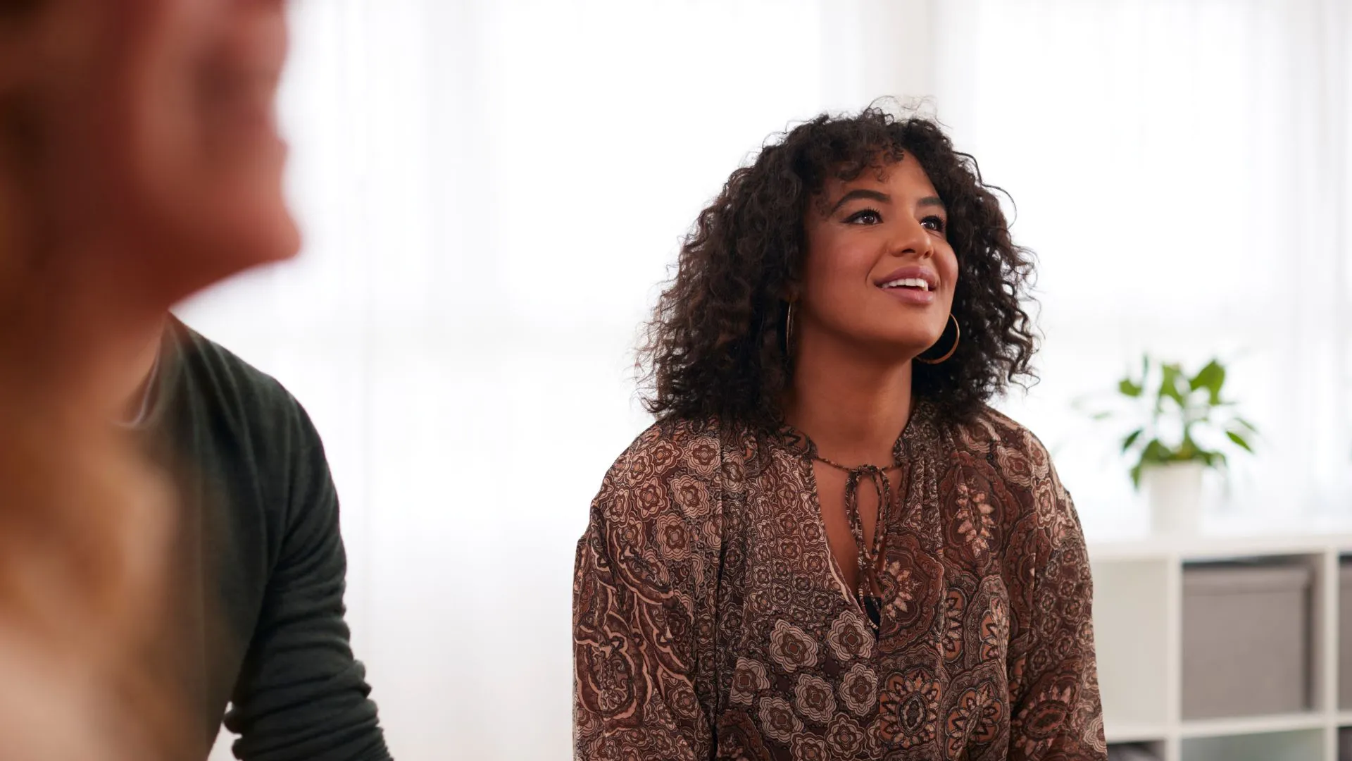 A woman with curly hair, wearing a patterned blouse, looks engaged and upbeat in a well-lit group setting. This scene represents ‘learning that works’ and underscores the power of ‘leading with emotional intelligence.’