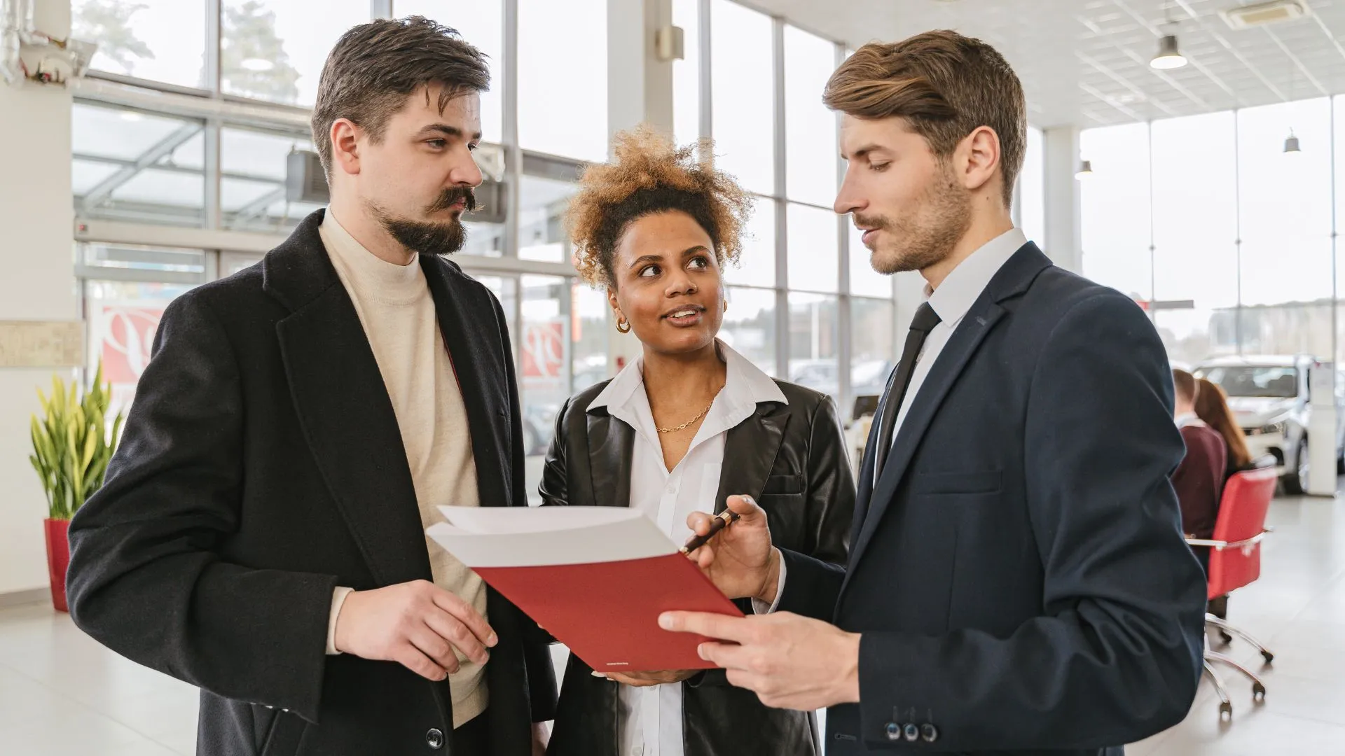 three colleagues are standing in a bright, open workspace discussing some documents one of them is holding.