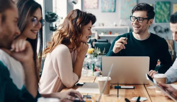 A group of colleagues are conversing and laughing around a conference table.