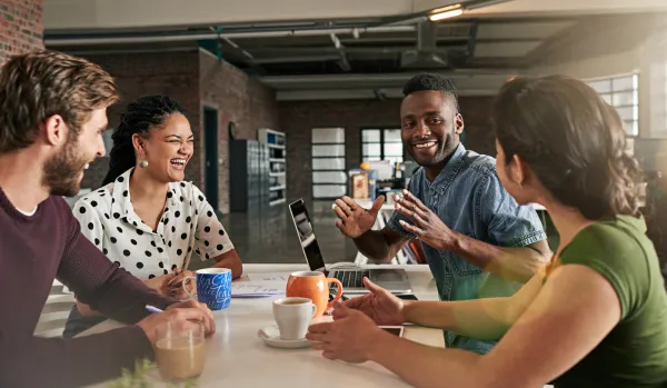 Four employees, working, sitting at a table in conversation, laughing and connecting.
