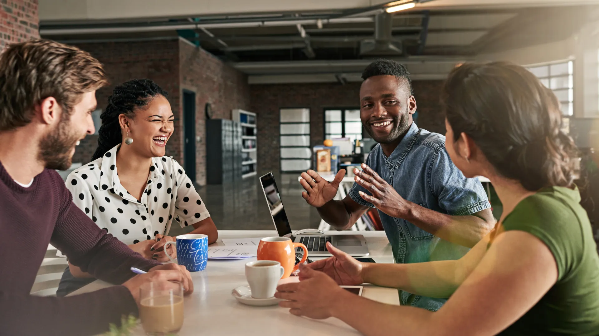 Four employees, working, sitting at a table in conversation, laughing and connecting.