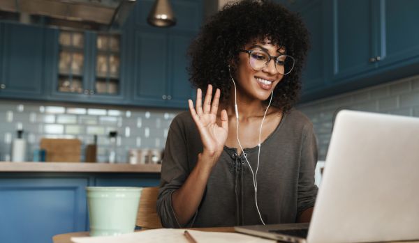 A woman is waving at her laptop as she participates in a virtual training program.