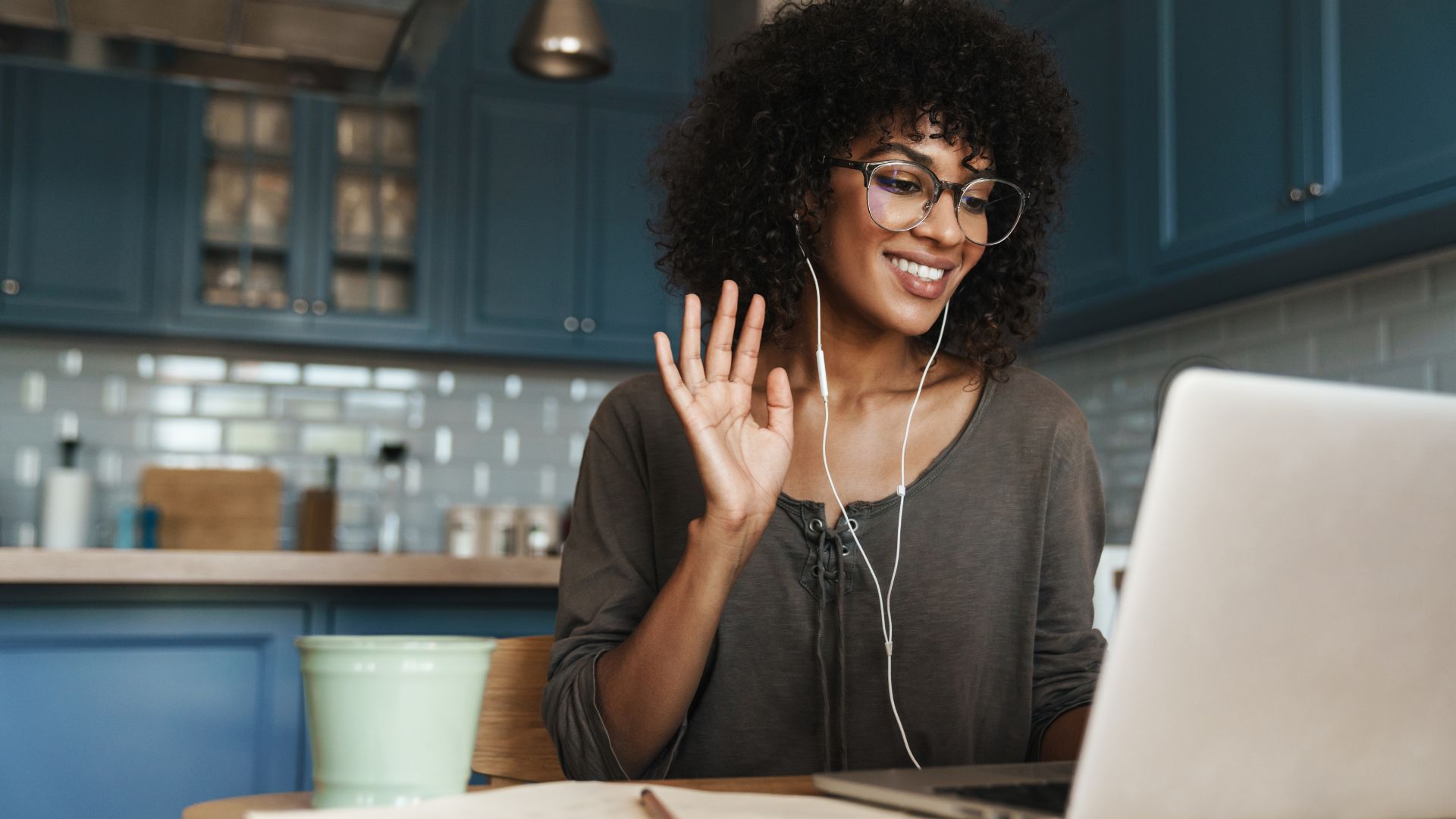 A woman is waving at her laptop as she participates in a virtual training program.