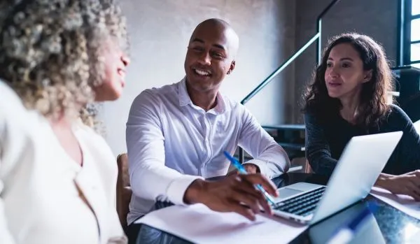 A diverse group of 3 people are working around a laptop in an office.