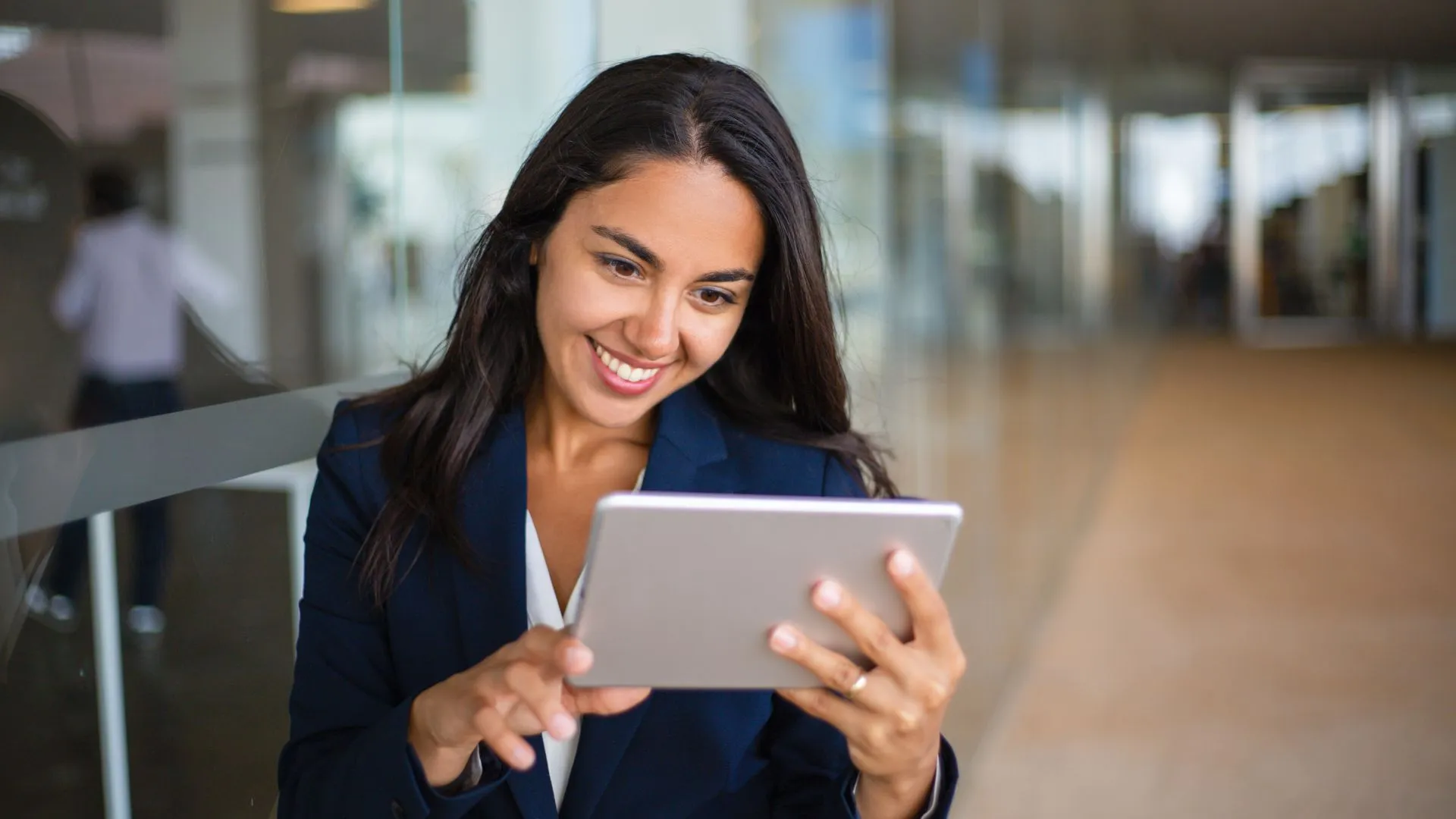 A young woman is smiling at her tablet in an open office space.