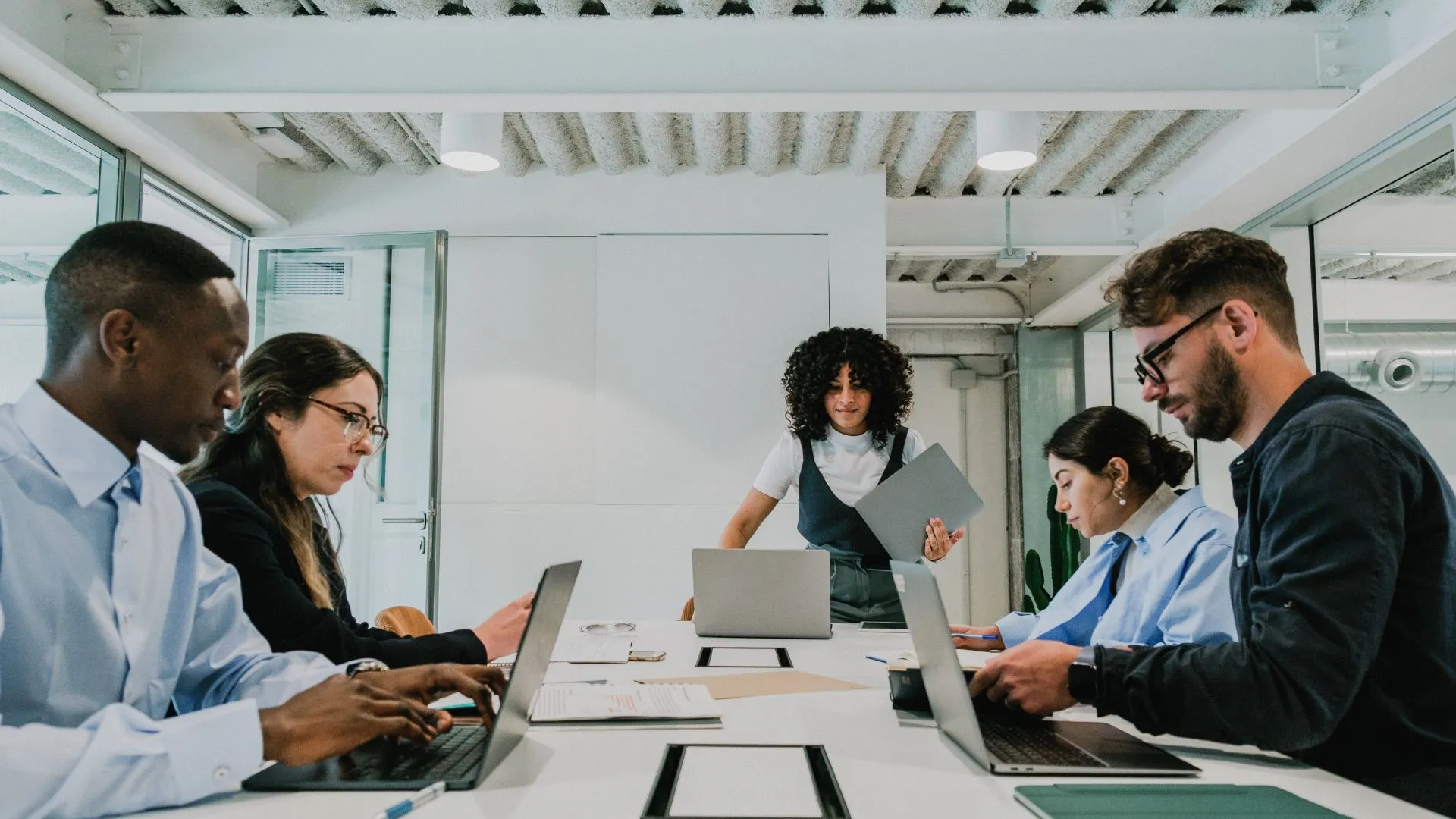 A team is quietly working around a conference table on their laptops.