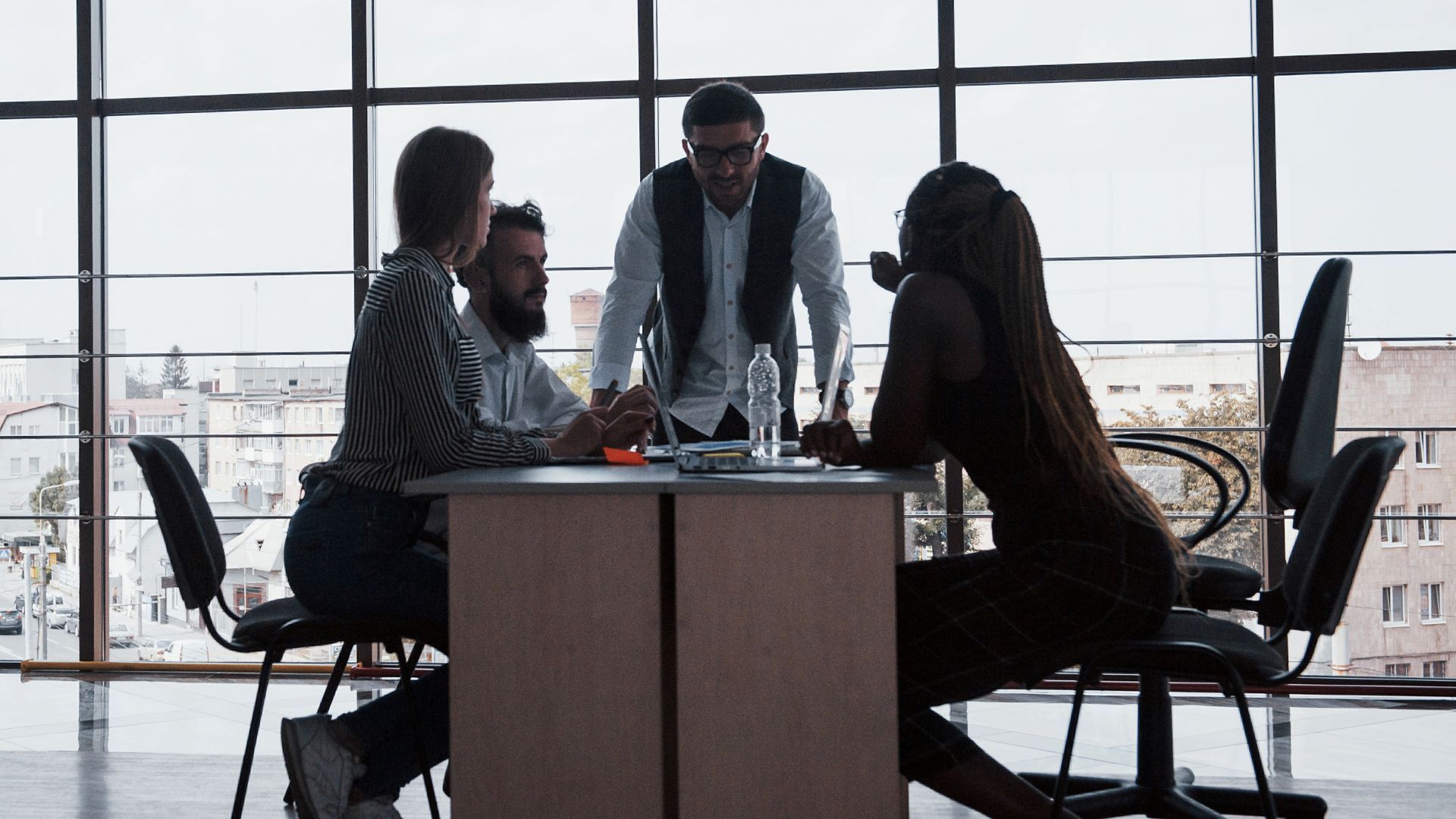 A diverse team is gathered around a table discussing a project. The person leading the conversation is standing and implementing skills learned in custom simulations.