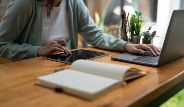 We're looking at someone's hands on their tablet and laptop at a table.