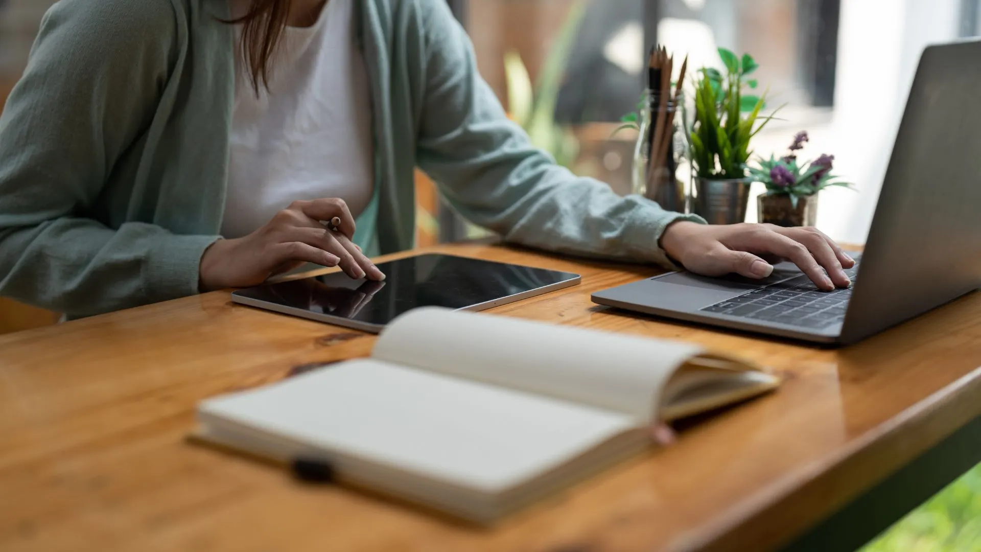 We're looking at someone's hands on their tablet and laptop at a table.