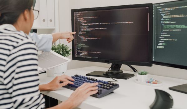 A woman is learning to code. A coworker we can't see is pointing at the woman's screen.