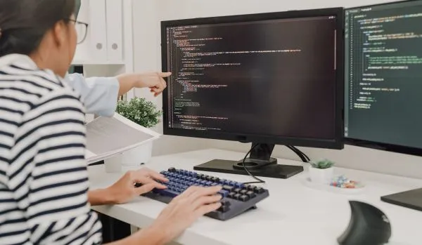 A woman is learning to code. A coworker we can't see is pointing at the woman's screen.