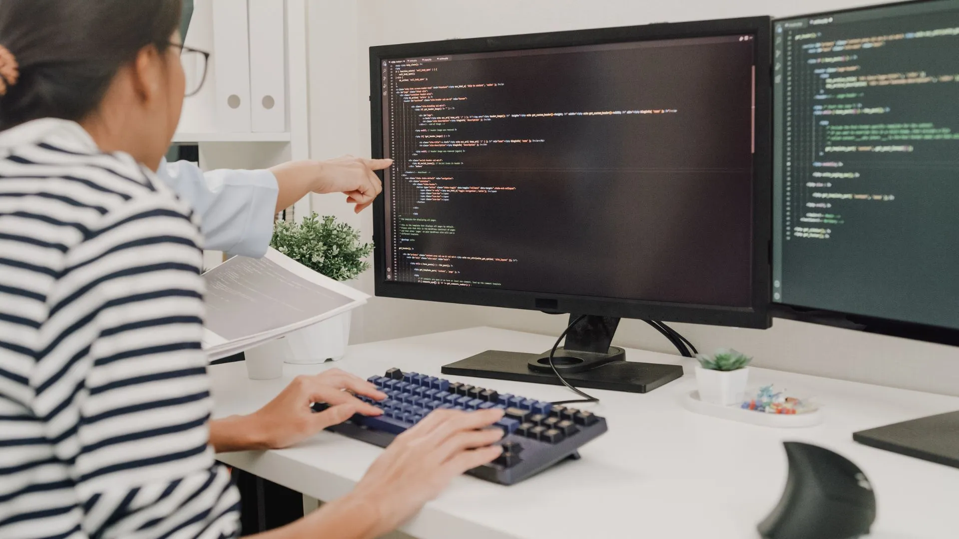 A woman is learning to code. A coworker we can't see is pointing at the woman's screen.