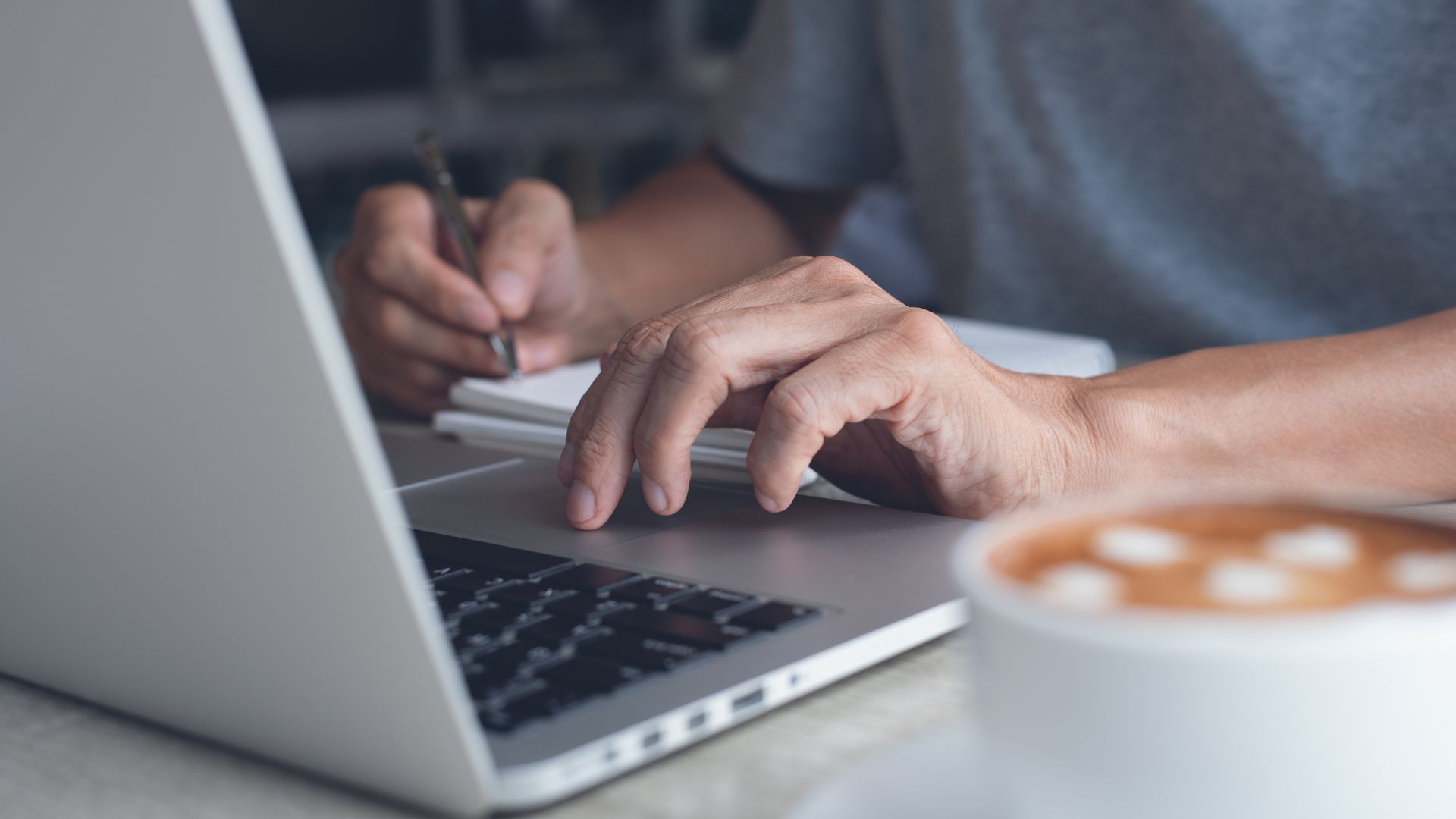 A close-up photo of someone's hands on their laptop with a cup of coffee in the foreground.