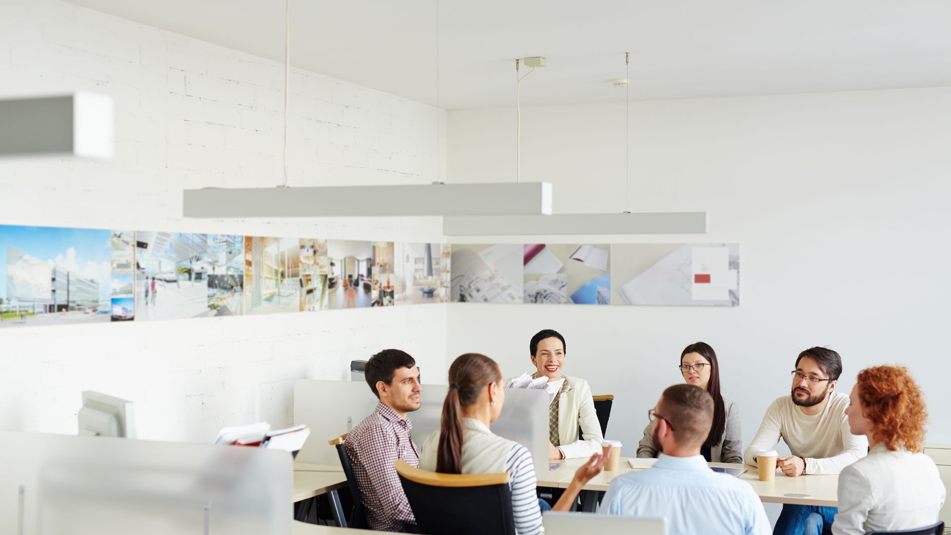 A diverse team of people are sitting around a table in a minimalist, modern office having a group conversation.