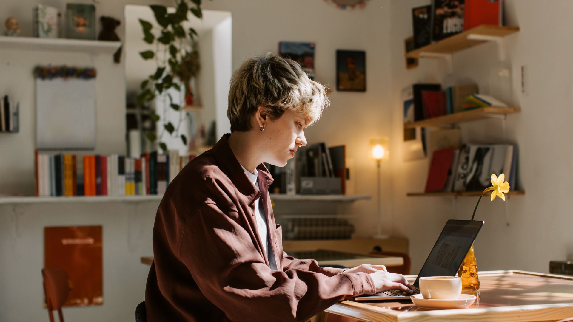 A person is sitting at a table in their apartment working on their laptop.