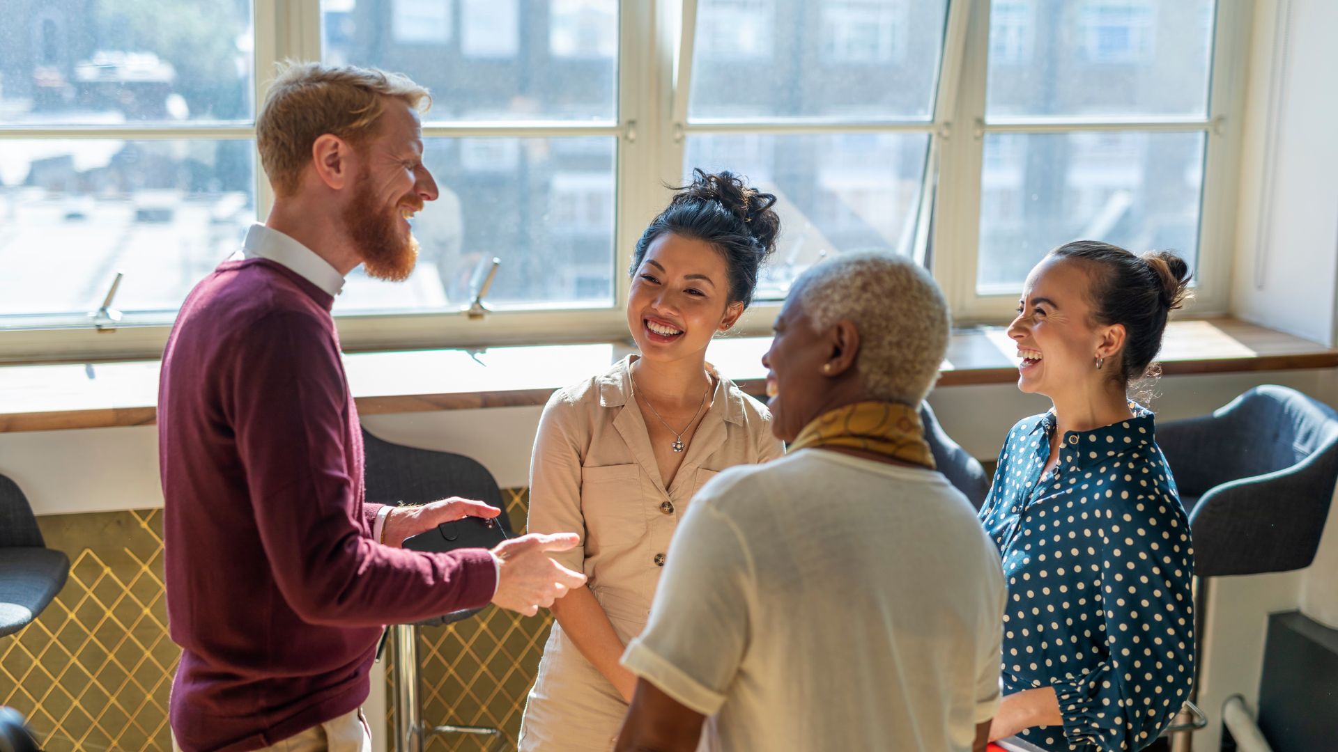 A diverse group of colleagues are standing in a common space, laughing and talking.