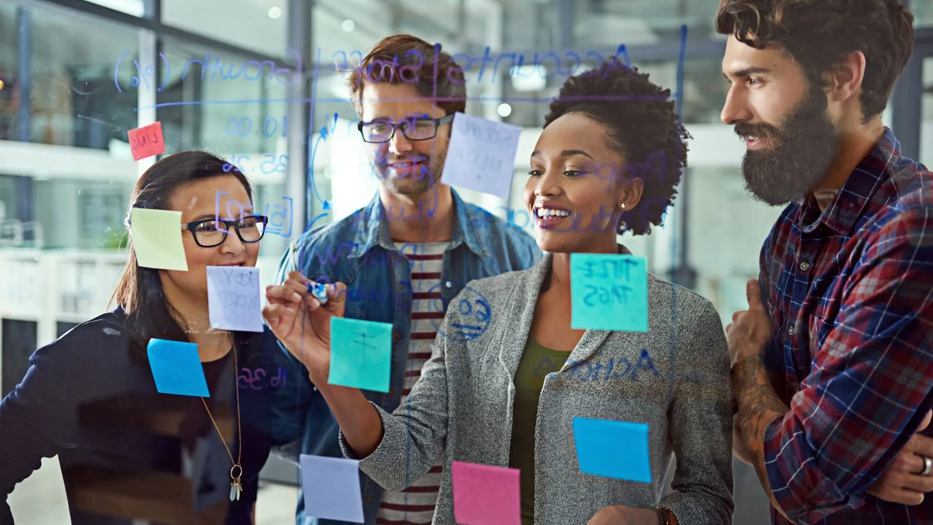 We're looking through a transparent whiteboard at a diverse learning and development team using markers and post-its to create a learning roadmap.