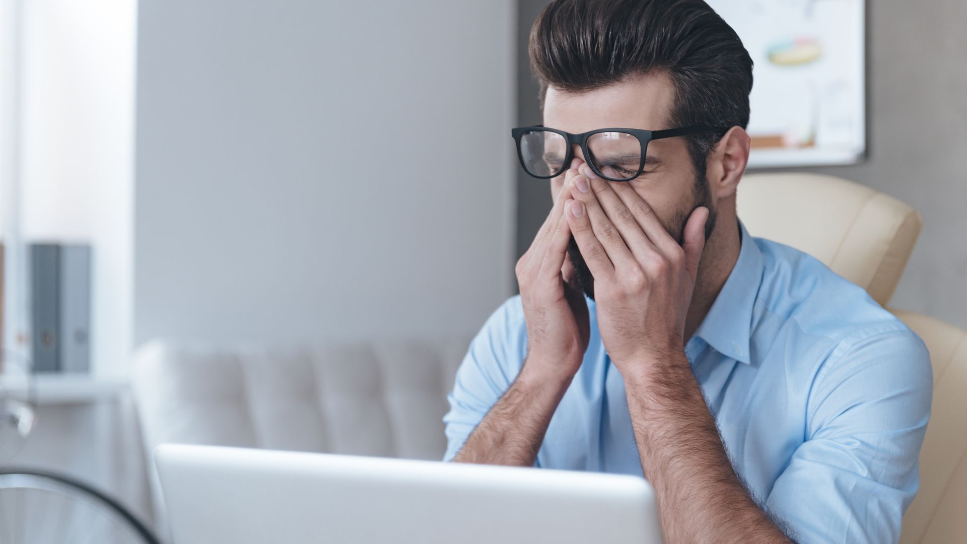 A tired manager is sitting at his desk, rubbing his eyes.