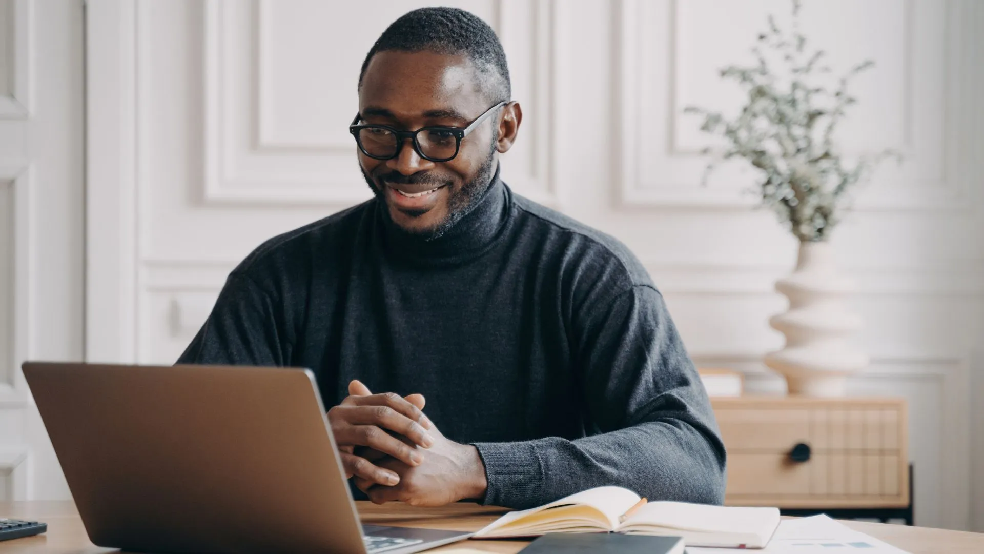 A happy remote worker is smiling down at his laptop.